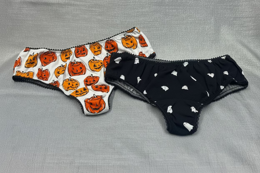 A set of two Halloween-themed panties. The first pair features a playful design with orange pumpkin faces, while the second pair is adorned with white bats on a black background, capturing the essence of Halloween.